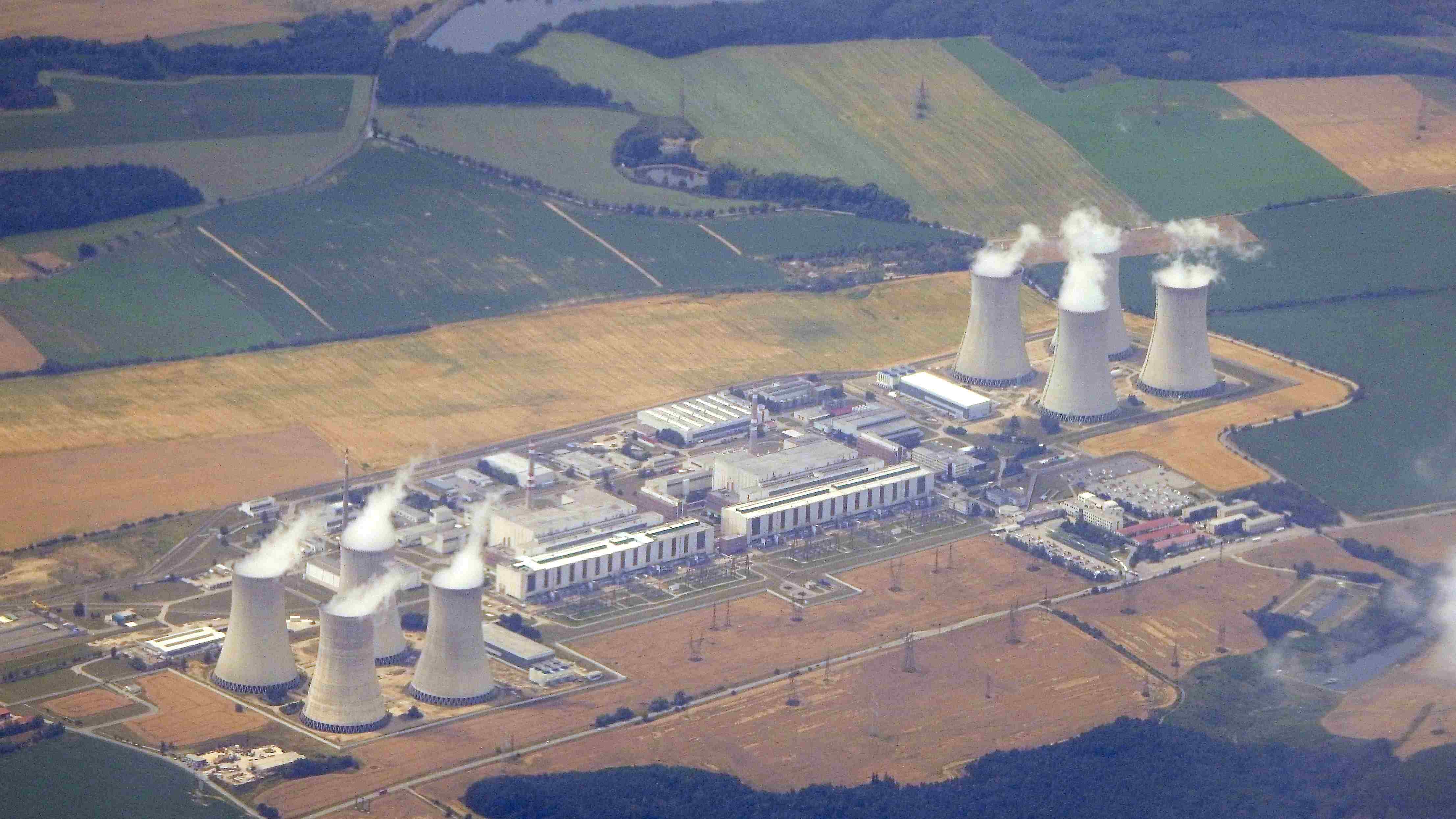 Luftaufnahme des Kernkraftwerks Dukovany in Tschechien mit mehreren Reaktor- und Kühlturmanlagen. Aus den Kühltürmen steigt Wasserdampf auf, die Anlage ist von Feldern und landwirtschaftlichen Flächen umgeben.