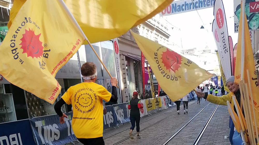 Marathon: Sportler läuft in gelbem Shirt mit Aufdruck "Klimaschutz mit AKW? So ein Schmäh!" und trägt wehende, gelbe Anti-Atom-Fahne